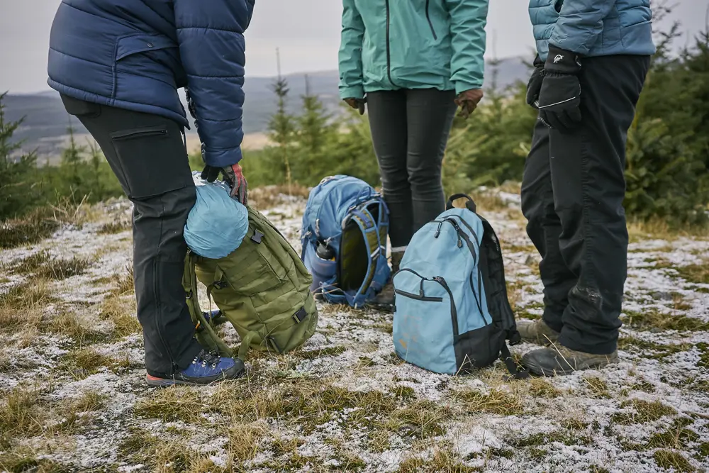 Three people with rucksacks, standing on a hill