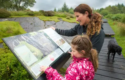 Woman and young girl in pink look at Rock Art interpretation board, Achnabreac