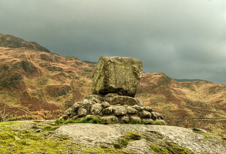 A large stone monument with a hill and walking trail behind
