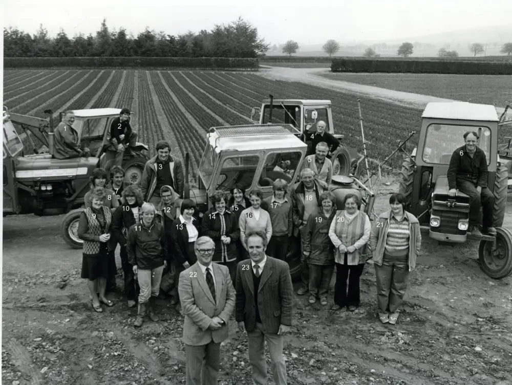 Black and white image of a group of people standing in front of neat fields