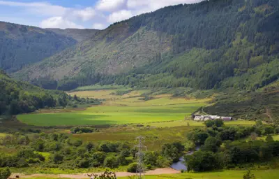 A semi wooded chain of hills with a valley of fields, houses, a small river, and power lines.