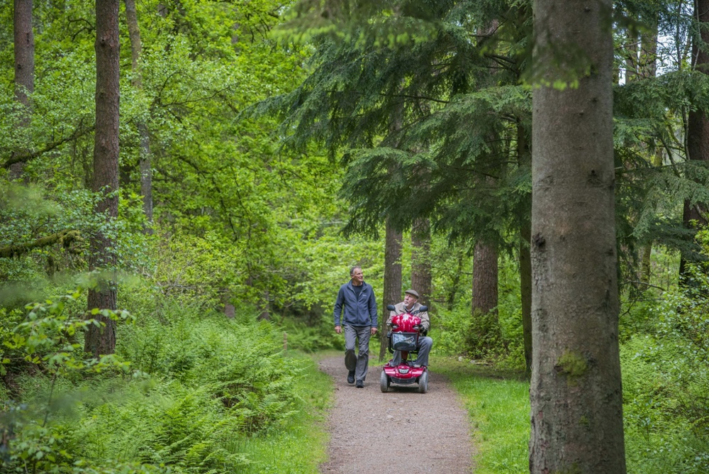 2 people on a trail with one on foot and the other person on a mobility scooter.