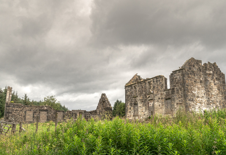 Old stone buildings in a field with trees behind