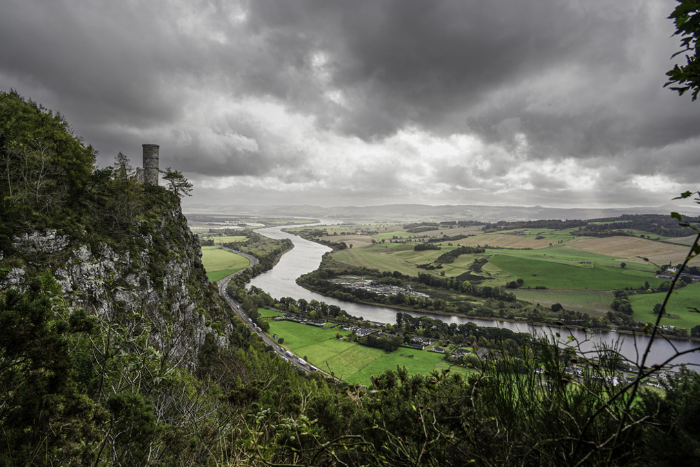 A cliff with a tower overlooking a river surrounded by fields